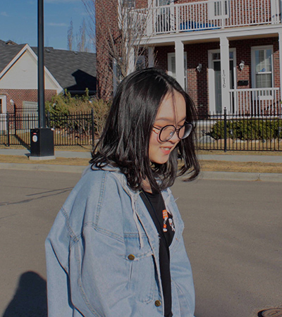 NAIT ESL student and bursary recipient walks outside wearing a denim jacket and wearing glasses.