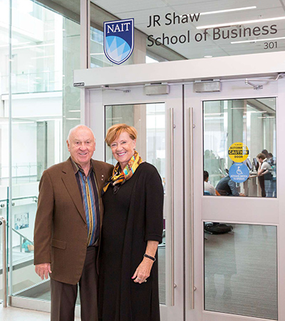 JR and Carol Shaw portrait in front of the doors to the JR Shaw School of Business at NAIT.