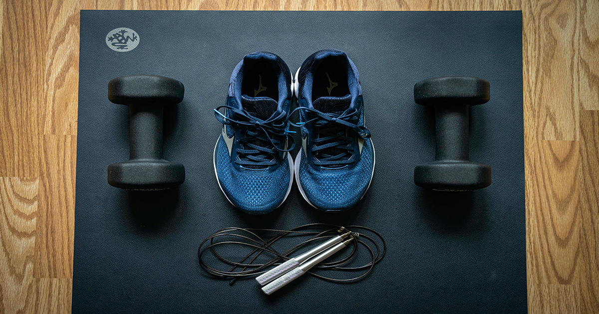 A pair of gym shoes, dumbells and a skipping rope placed on top of a yoga mat.