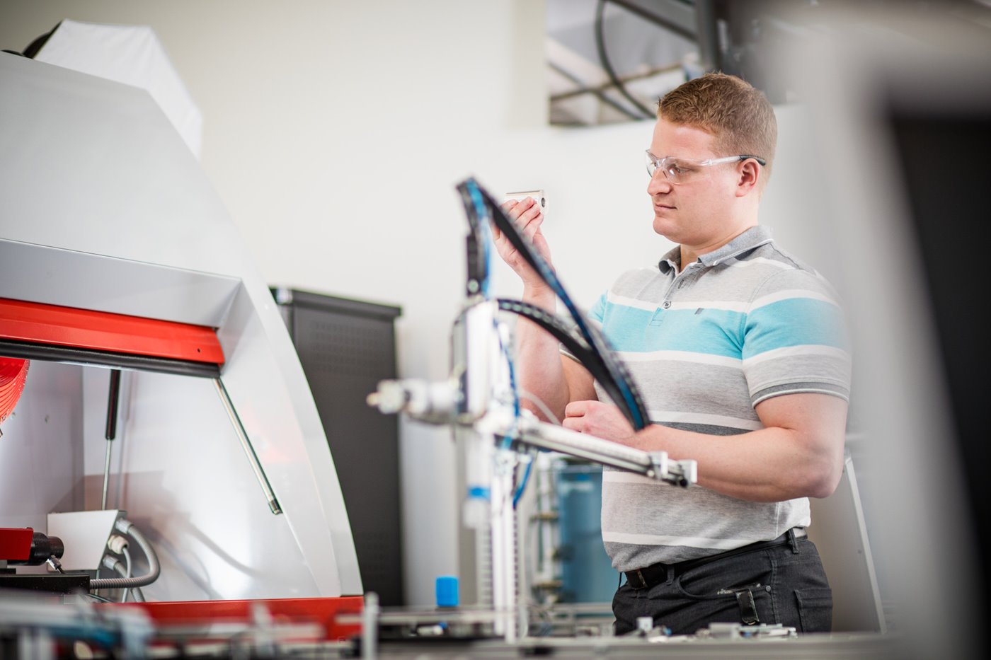 A man wearing safety goggles inspects a cylindrical piece of metal
