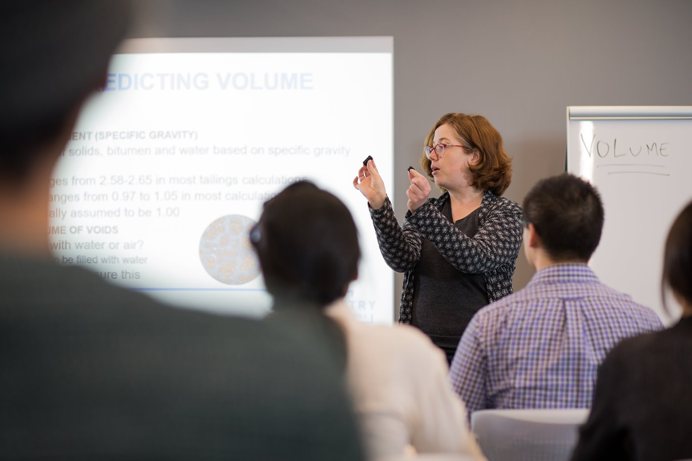 a teacher at the front of a class room using blocks to illustrate a lesson on clays