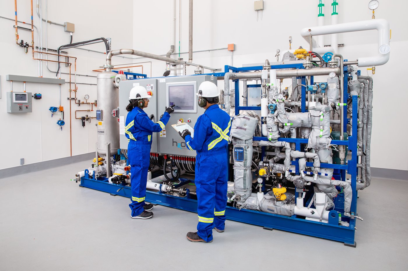 Two people in safety equipment stand in front of a membrane testing machine
