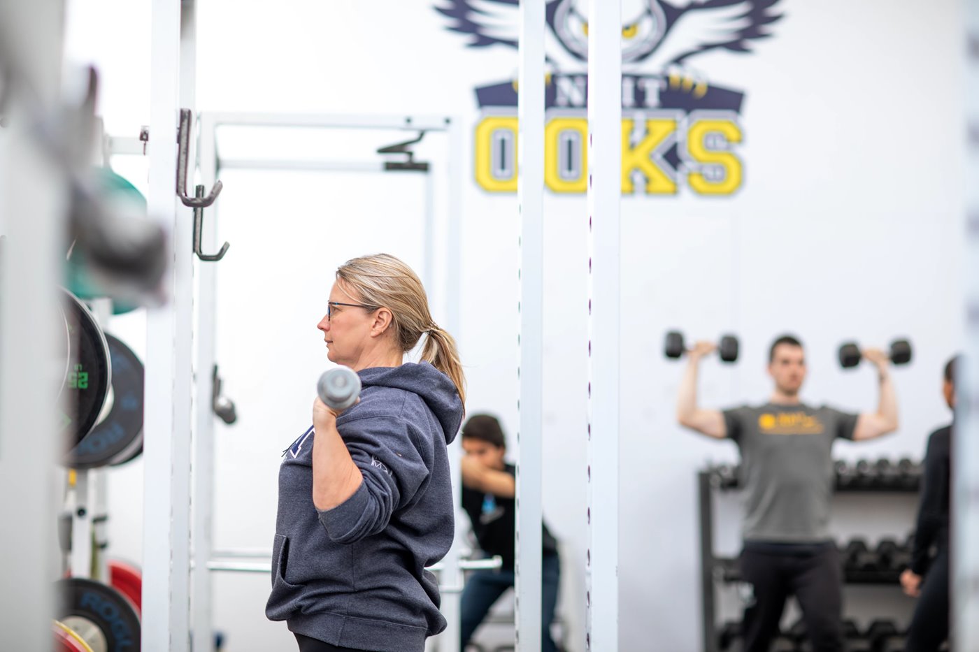 Woman stands in a weights centre holding a barbell up below her chin